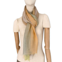 Mannequin wearing an elegant hand-painted Otta wool silk blend scarf on a white background. Warm green, orange and beige tones.
