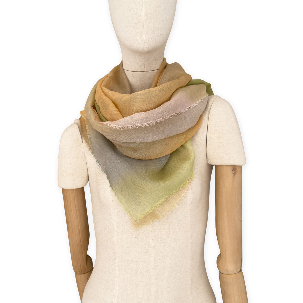 Mannequin wearing an elegant hand-painted Otta wool silk blend scarf on a white background. Warm green, orange and beige tones.
