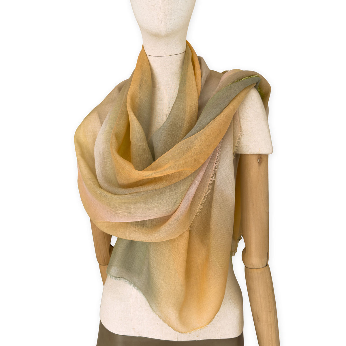 Mannequin wearing an elegant hand-painted Otta wool silk blend scarf on a white background. Warm green, orange and beige tones.
