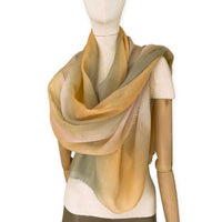 Mannequin wearing an elegant hand-painted Otta wool silk blend scarf on a white background. Warm green, orange and beige tones.
