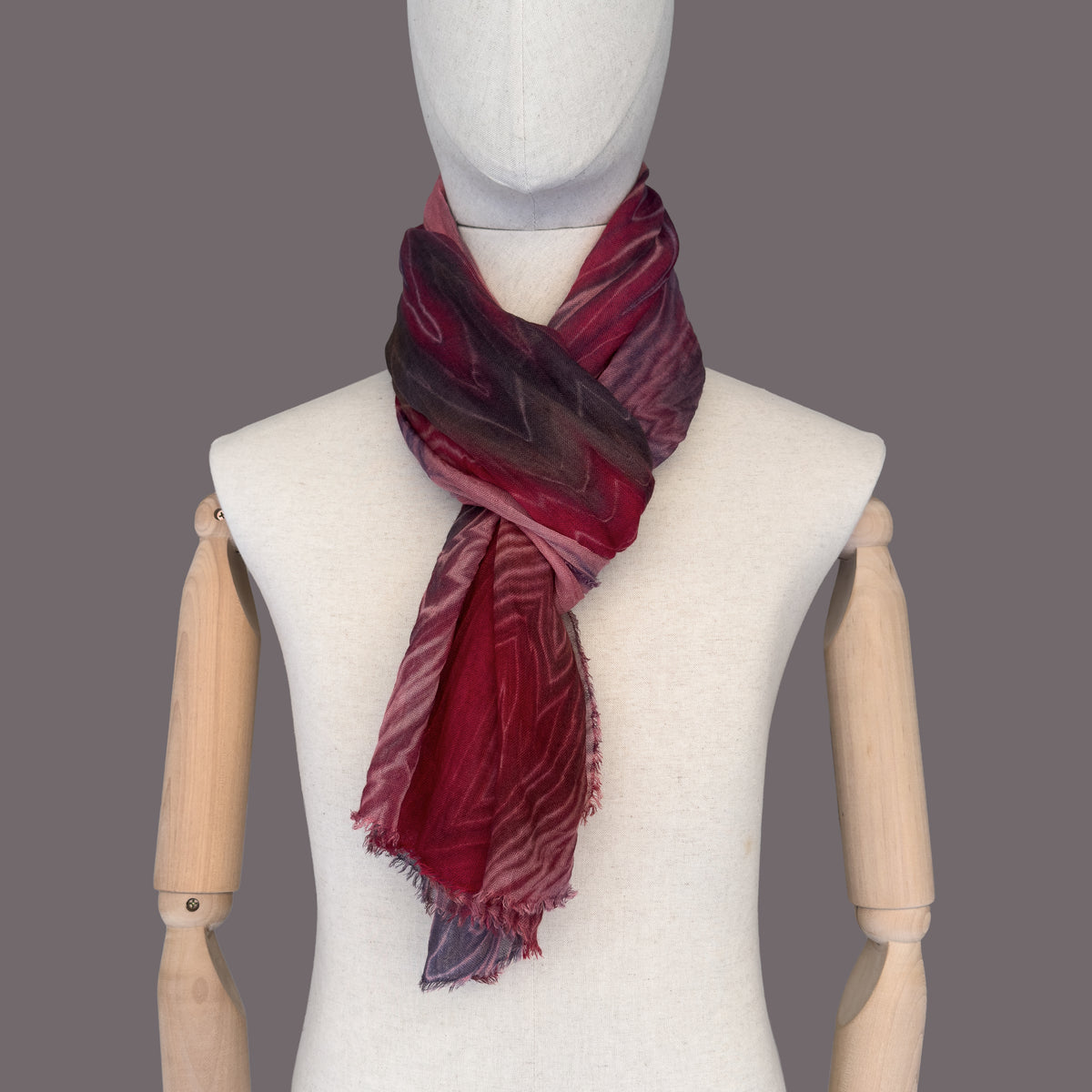 Mannequin wearing scarf on a gray background. Hand-painted wool & silk scarf by Otta-Italy, 54 x 193 cm, featuring 
red, purple and dark gray. Luxury Italian wool & silk accessory, soft and warm scarf for women and men.
