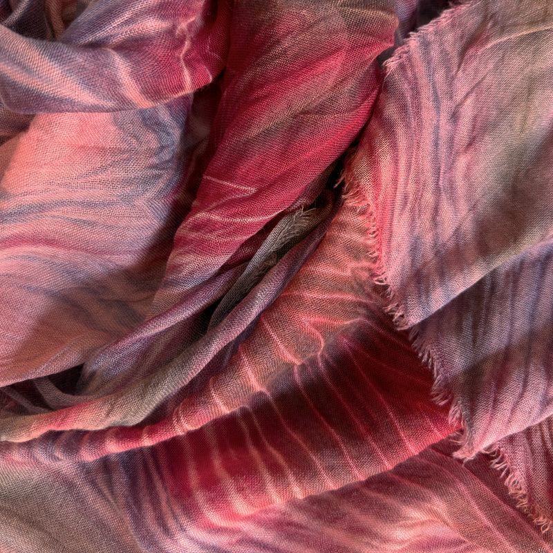 Close-up of a hand-painted Otta wool & silk scarf draped softly, showcasing gentle shades of 
red, purple and dark gray. Lightweight artisan accessory with delicate hand-fringed edges, measuring 54 x 193 cm.
